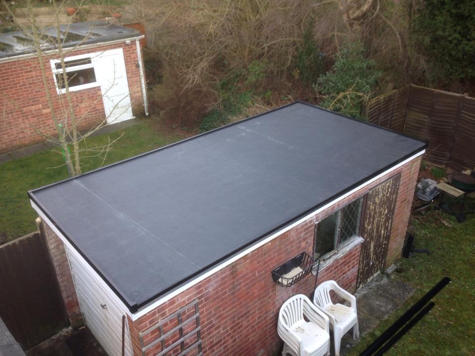 A black rubber flat roof fitted on a brick outbuilding, viewed from above with garden chairs below.