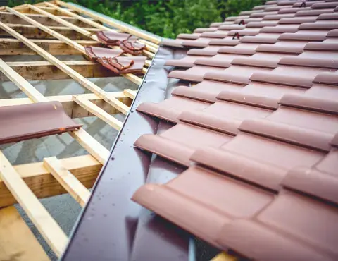 Close-up of brown interlocking concrete roof tiles being laid over timber roof battens.