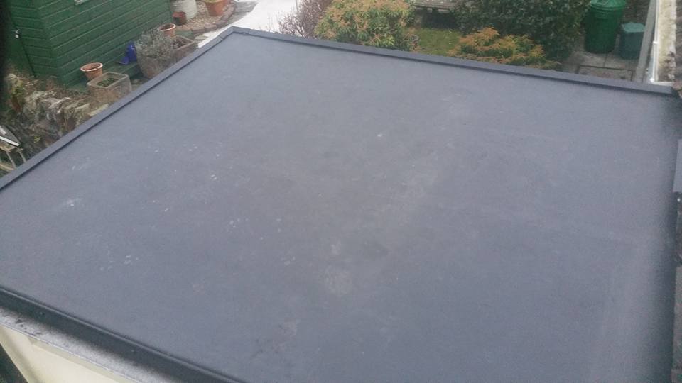 A close-up view of a dark grey EPDM rubber flat roof overlooking a back garden.