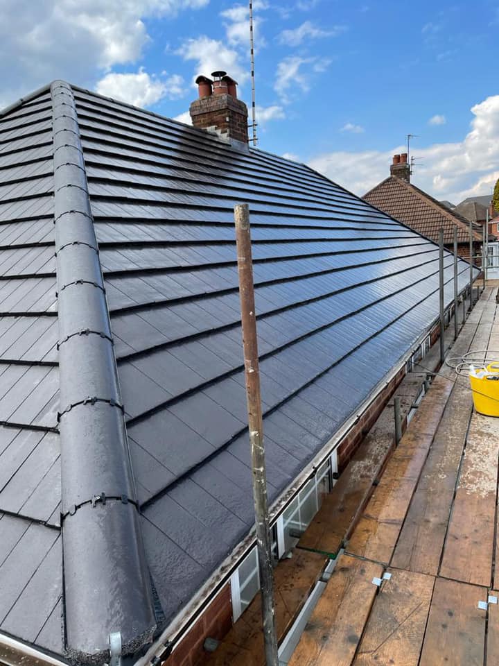 A steeply pitched dark grey concrete tiled roof with a brick chimney stack under a blue sky.