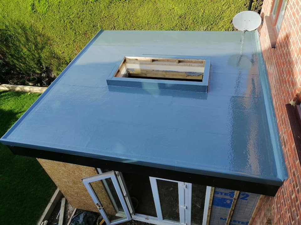 A newly installed grey GRP fibreglass flat roof on a garden building, with an open timber-framed skylight aperture and a satellite dish on the adjoining brick wall.