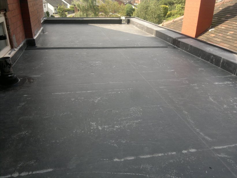 A grey EPDM rubber flat roof surrounding a brick chimney stack with rooftops visible in the background.