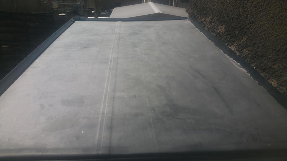 A close-up view of a smooth grey EPDM rubber flat roof membrane installed on a house extension.