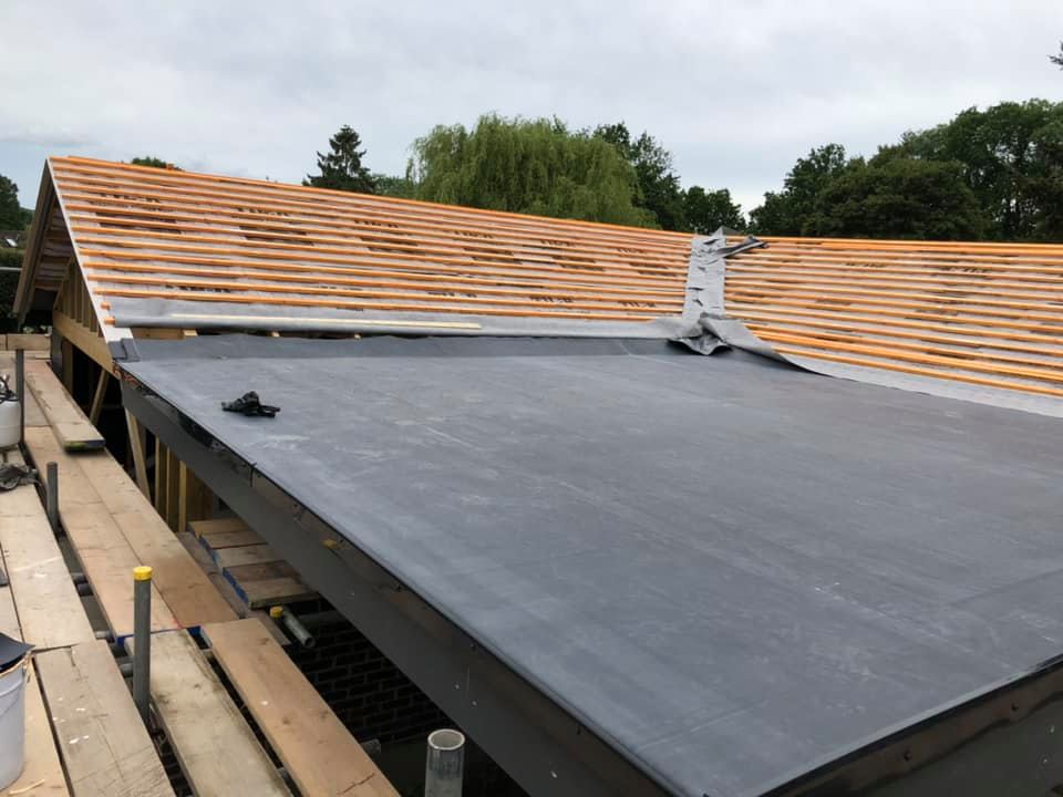 A new dark grey flat rubber roof partially installed beneath exposed timber rafters during a roofing job.