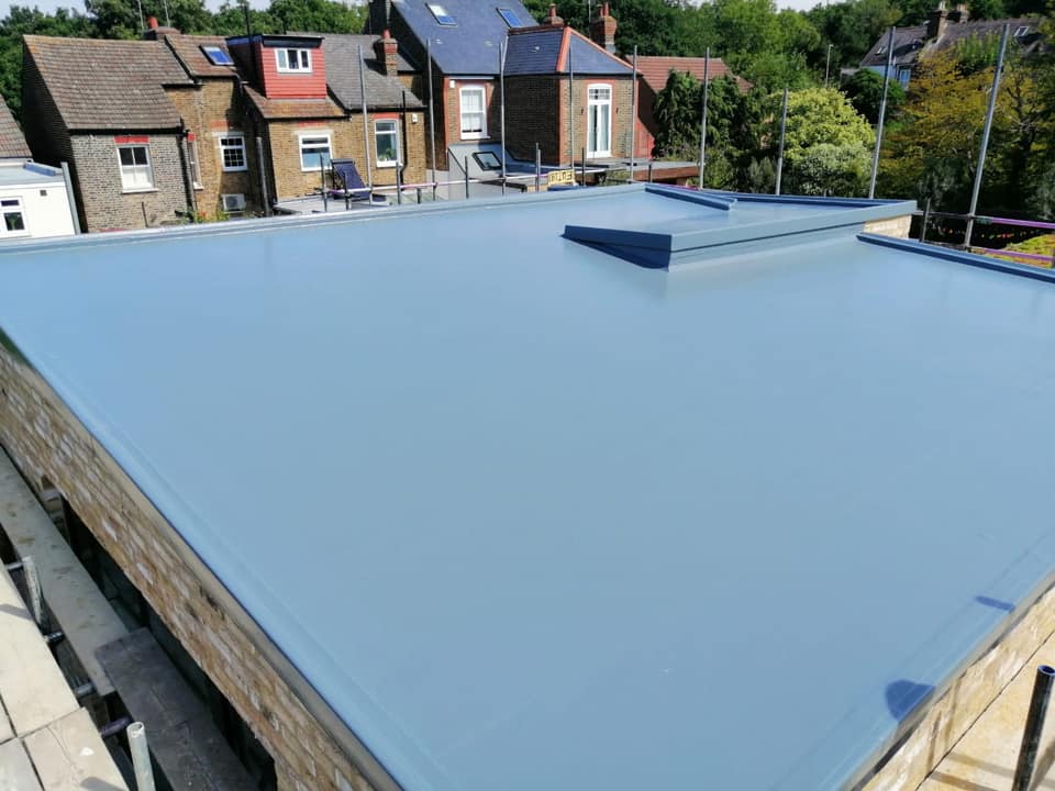 A pale blue-grey fibreglass flat roof on a house extension with a raised skylight and surrounding rooftops visible.
